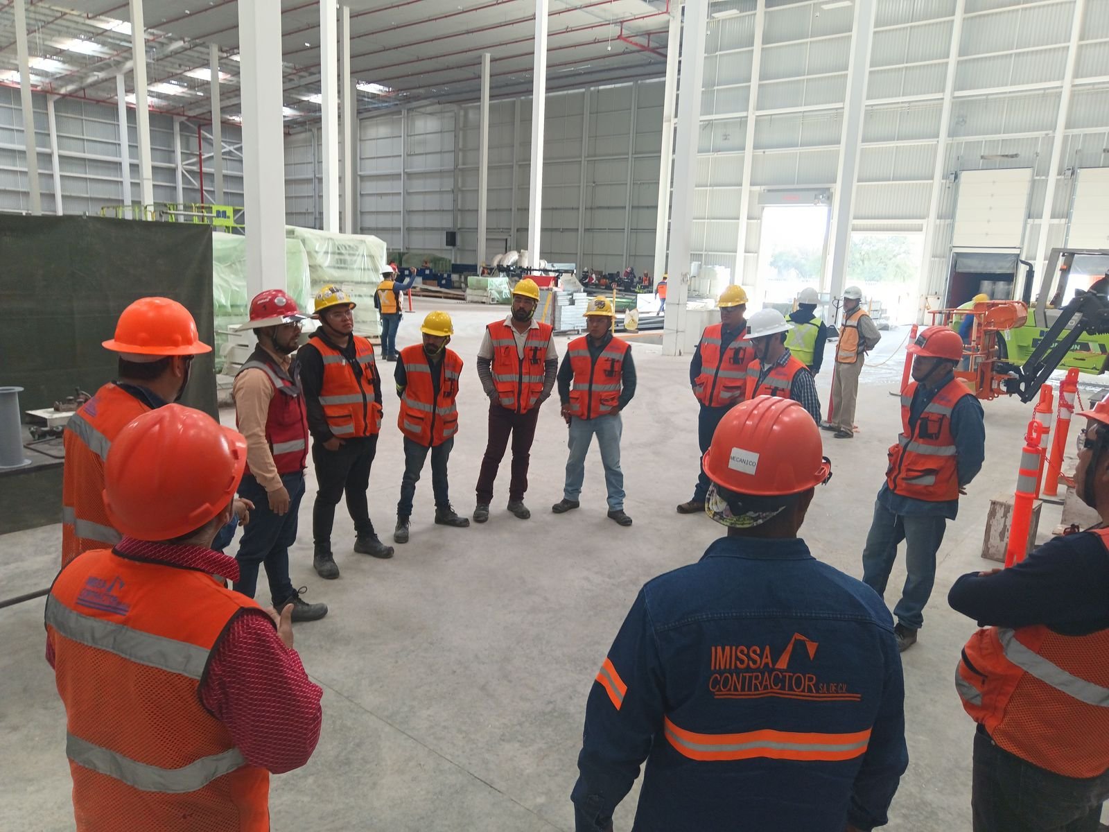 Personal de IMISSA con cascos y chalecos reunido en círculo dentro de una nave industrial